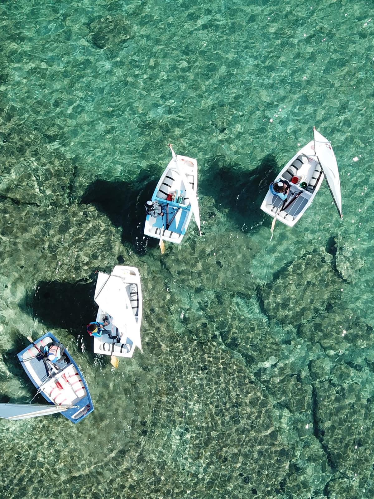 Aerial view of four sailing dinghies with white sails on clear turquoise water